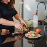 Un cuplu care gătește împreună în bucătăria de acasă, zâmbind și împărțind sarcinile